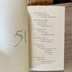 Pu&ograve; includere: Pagine di un libro aperto con una poesia e il numero 51 in grigio. La poesia include frasi come &laquo;Non ho bisogno di altre parole&raquo; e &laquo;Non ho bisogno di pi&ugrave; tempo&raquo;. Le pagine sono su una superficie di legno chiaro.