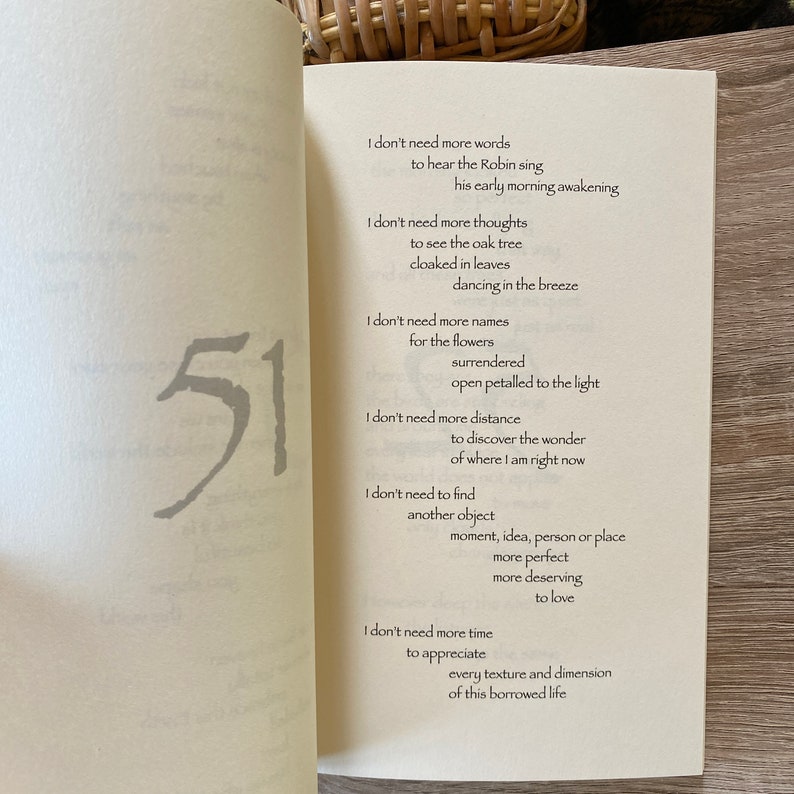Pu&ograve; includere: Pagine di un libro aperto con una poesia e il numero 51 in grigio. La poesia include frasi come &laquo;Non ho bisogno di altre parole&raquo; e &laquo;Non ho bisogno di pi&ugrave; tempo&raquo;. Le pagine sono su una superficie di legno chiaro.
