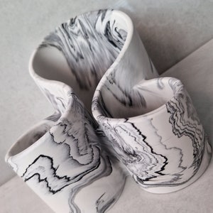 May include: A white ceramic organiser with a black marbled design. The organiser has three compartments and is shaped like a swirl.