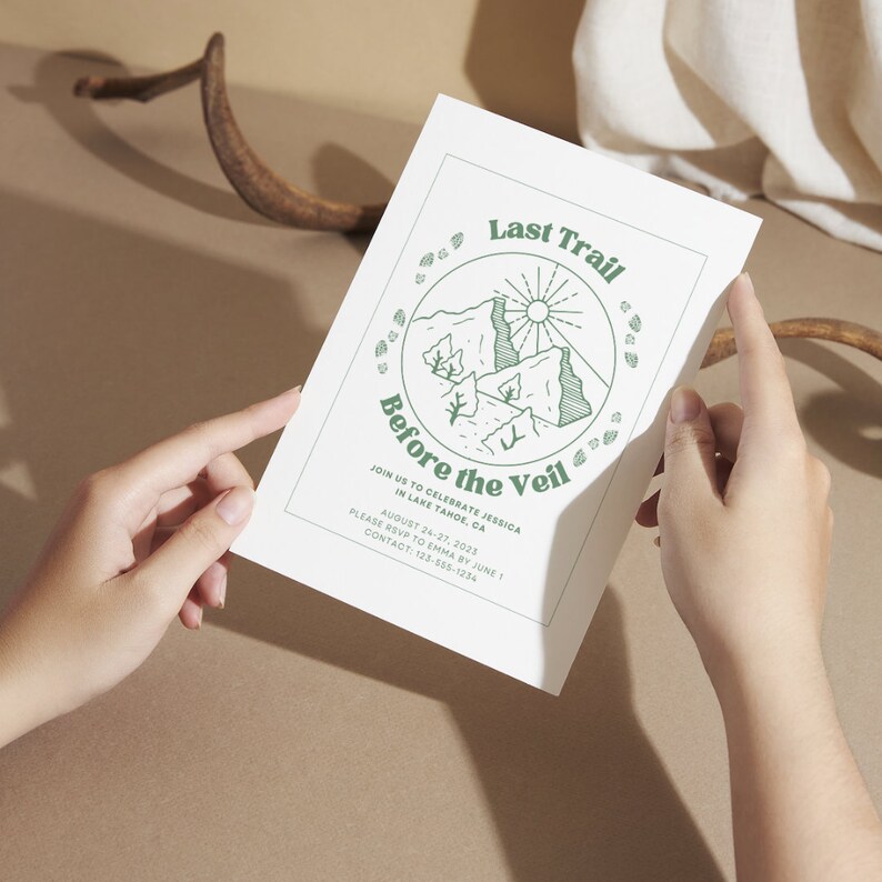 May include: A white invitation card with green text and a line drawing of a mountain landscape. The text reads "Last Trail Before the Veil" and includes details about a wedding celebration in Lake Tahoe, California. The invitation requests RSVP by June 1st.