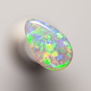 Könnte beinhalten: Ein tropfenförmiger Opal-Edelstein mit einer weißen Basis und schillernden grünen, blauen und gelben Blitzen.