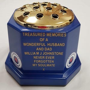May include: A blue hexagonal memorial flower vase with a gold-coloured metal top featuring multiple circular openings. The front displays gold text reading: TREASURED MEMORIES OF A WONDERFUL HUSBAND AND DAD WILLIAM J JOHNSTONE NEVER EVER FORGOTTEN MY SOULMATE X.
