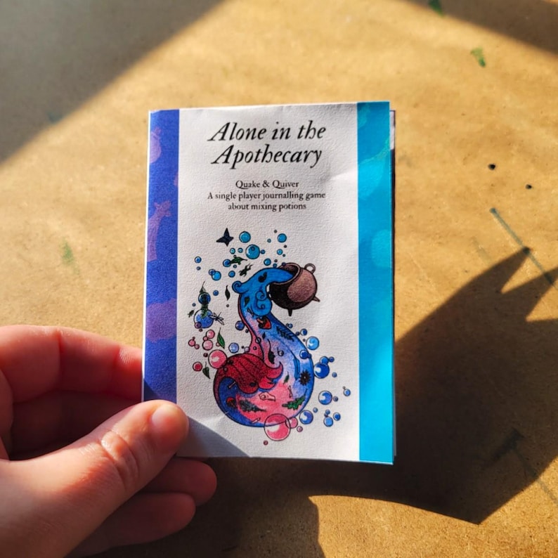 Może przedstawiać: Mała książeczka zatytułowana "Alone in the Apothecary" z tekstem "Quake & Quiver" i "A single player journalling game about mixing potions". Okładka zawiera kolorową ilustrację butelki z miksturą z niebieskimi, r&oacute;żowymi i brązowymi akcentami.