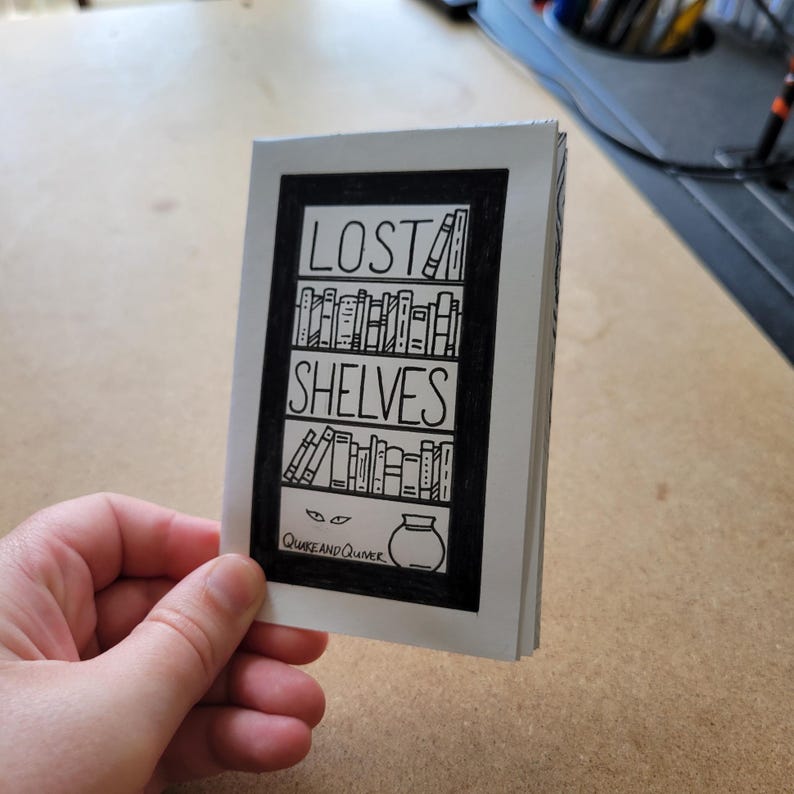 May include: A black and white illustration of a bookshelf with the words "LOST SHELVES" above it. The illustration includes a pair of eyes peeking out from below the bottom shelf and a jar with a lid on top of the shelf. The text "Quirk and Quimer" is below the illustration.
