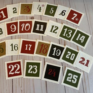 May include: Advent calendar cards with scalloped edges, numbered 1-25. The cards feature various colors, including red, green, brown, and black, with white numbers. Some cards have snowflake accents. A festive holiday decoration.