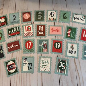 May include: A collection of 25 Christmas-themed advent calendar cards. Each card has a scalloped edge and features a number or word, along with festive illustrations like Santa, a snowman, and a Christmas tree.