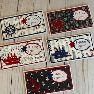 May include: A collection of nautical-themed "Thank You" cards. Each card features a different design, including anchors, ships, and steering wheels, in red, white, and blue. The cards have a white border and are set against a light wood grain background.