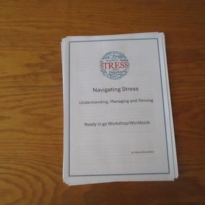May include: A white booklet titled "Navigating Stress: Understanding, Managing and Thriving" with a blue circle containing the word "STRESS" in red letters. The booklet is a "Ready to go Workshop/Workbook".