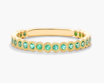 Puede incluir: Un delicado anillo de banda de oro con una fila de piedras preciosas verdes engastadas en un diseño festoneado.