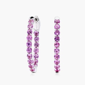 May include: A pair of silver hoop earrings with a row of pink sapphires around the outside of each hoop.