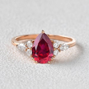 May include: A pear-shaped ruby engagement ring set in rose gold with a halo of smaller diamonds.