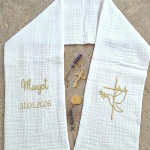 May include: White baptismal stole with gold embroidery. The stole features the name "Margot" and the date "31.01.2026". A gold cross and a dove with an olive branch are also embroidered on the stole. The stole is made of a textured fabric.