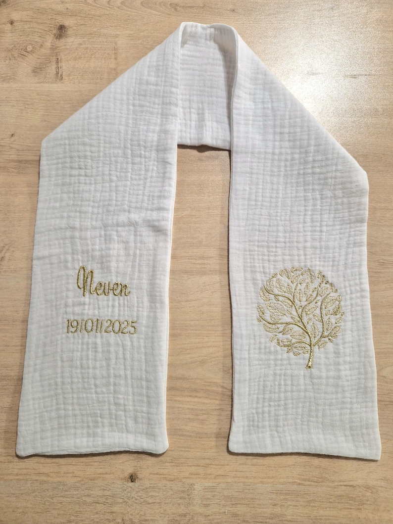 May include: White scarf with a textured weave. The scarf features embroidered text that reads "Never" above the date "19/01/2025" and a gold tree design. The scarf is made of a soft, lightweight fabric.
