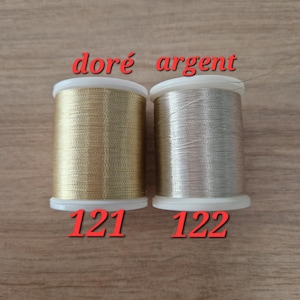 May include: Two spools of metallic thread, one gold and one silver, are displayed. The gold spool is labeled "121" and the silver spool is labeled "122". The words "dor&eacute; argent" are written above the spools.