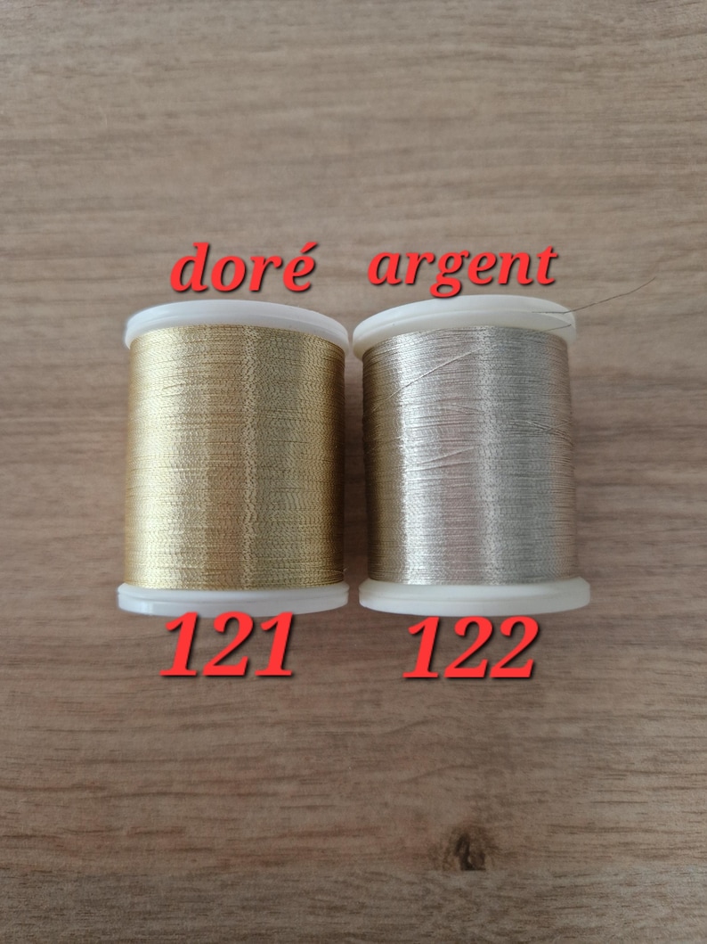 May include: Two spools of metallic thread, one gold and one silver, are displayed. The gold spool is labeled "121" and the silver spool is labeled "122". The words "dor&eacute; argent" are written above the spools.