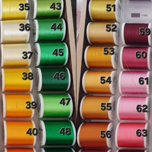 May include: A wooden box filled with spools of thread in various colors. The thread colors range from yellow and green to orange, red, and purple. Each spool is labeled with a number from 34 to 64.