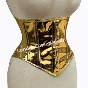 Puede incluir: Un cors&eacute; met&aacute;lico dorado con la parte inferior puntiaguda y cierre de busk. El cors&eacute; tiene un acabado brillante y est&aacute; hecho de una tela suave. El texto "LondonCorsetQueen" es visible en la parte delantera del cors&eacute;.