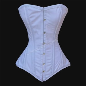 May include: A white corset with a structured, boned design. The garment features a series of metal clasps down the front and delicate trim along the top and bottom edges. The corset is designed to cinch the waist and create an hourglass figure.
