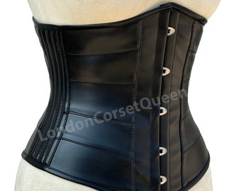 May include: A black corset with a structured design, featuring horizontal panels and vertical ribbing. The corset has a curved shape and is fastened with silver-colored clasps. The product is displayed on a mannequin.