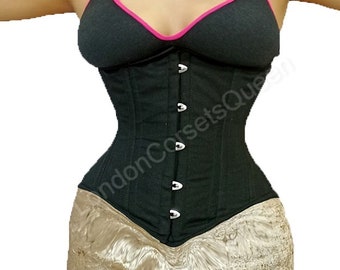 May include: A black cotton corset with silver metal busk closures and a pink trim on the straps. The corset is being worn over a black sports bra.