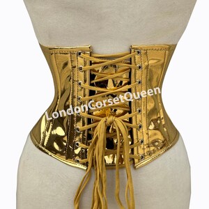 Puede incluir: Cors&eacute; de color dorado con lazada en la espalda y cierre de metal. El cors&eacute; est&aacute; hecho de una tela brillante y met&aacute;lica. Los cordones son de color marr&oacute;n claro. El texto "LondonCorsetQueen" est&aacute; impreso en la parte posterior del cors&eacute;.