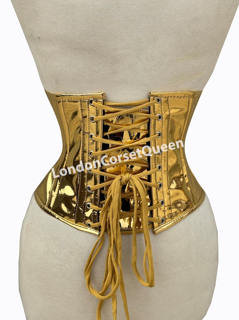 Puede incluir: Cors&eacute; de color dorado con lazada en la espalda y cierre de metal. El cors&eacute; est&aacute; hecho de una tela brillante y met&aacute;lica. Los cordones son de color marr&oacute;n claro. El texto "LondonCorsetQueen" est&aacute; impreso en la parte posterior del cors&eacute;.