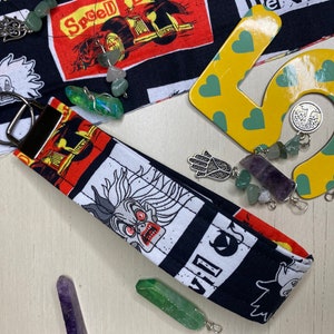 Pu&ograve; includere: Un portachiavi in tessuto bianco e nero con un personaggio dei cartoni animati con occhi rossi e una grande bocca. Il portachiavi ha un anello portachiavi argentato ed &egrave; decorato con una variet&agrave; di cristalli e ciondoli colorati.