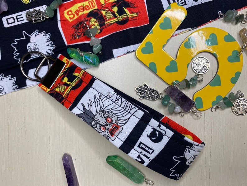 Pu&ograve; includere: Un portachiavi in tessuto bianco e nero con un personaggio dei cartoni animati con occhi rossi e una grande bocca. Il portachiavi ha un anello portachiavi argentato ed &egrave; decorato con una variet&agrave; di cristalli e ciondoli colorati.