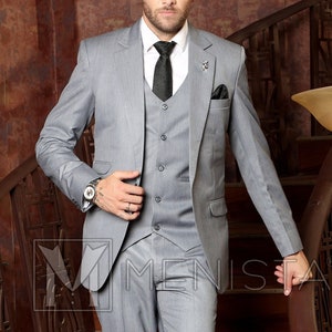 May include: A man wearing a gray suit with a vest and a black tie. He is standing on a staircase with a wooden railing.