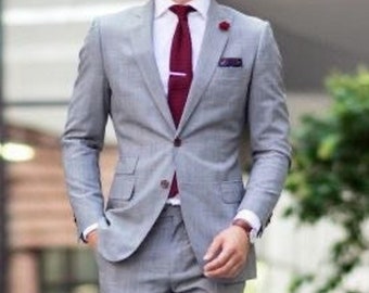 May include: A man wearing a gray suit with a burgundy tie and a gray fedora hat. He is wearing brown leather shoes with blue socks. The man is walking on a sidewalk.