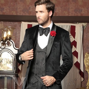 May include: A man wearing a black velvet tuxedo jacket with a satin lapel, a grey patterned waistcoat, black trousers, and black lace-up shoes. He is wearing a black bow tie and a red rose buttonhole.