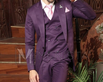 May include: A man wearing a purple three-piece suit with a pink patterned tie and black shoes. He is standing on a staircase with a plant in a pot to the right.