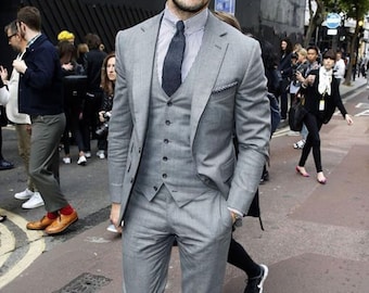 Puede incluir: Un hombre con un traje gris de tres piezas, corbata azul oscuro y zapatos de cuero marrón. Lleva gafas de sol y barba.