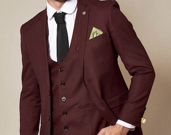 May include: A three-piece suit in a deep burgundy colour. The suit includes a jacket, waistcoat, and trousers. The jacket has a single button fastening and a pocket square. The waistcoat has a button fastening and five buttons. The trousers have a straight leg.