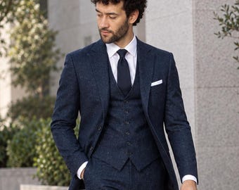 May include: A three-piece navy blue suit with a subtle speckled texture, consisting of a single-breasted blazer, a matching button-up vest, and trousers. The outfit includes a crisp white collared shirt, a dark navy tie, and brown leather shoes.