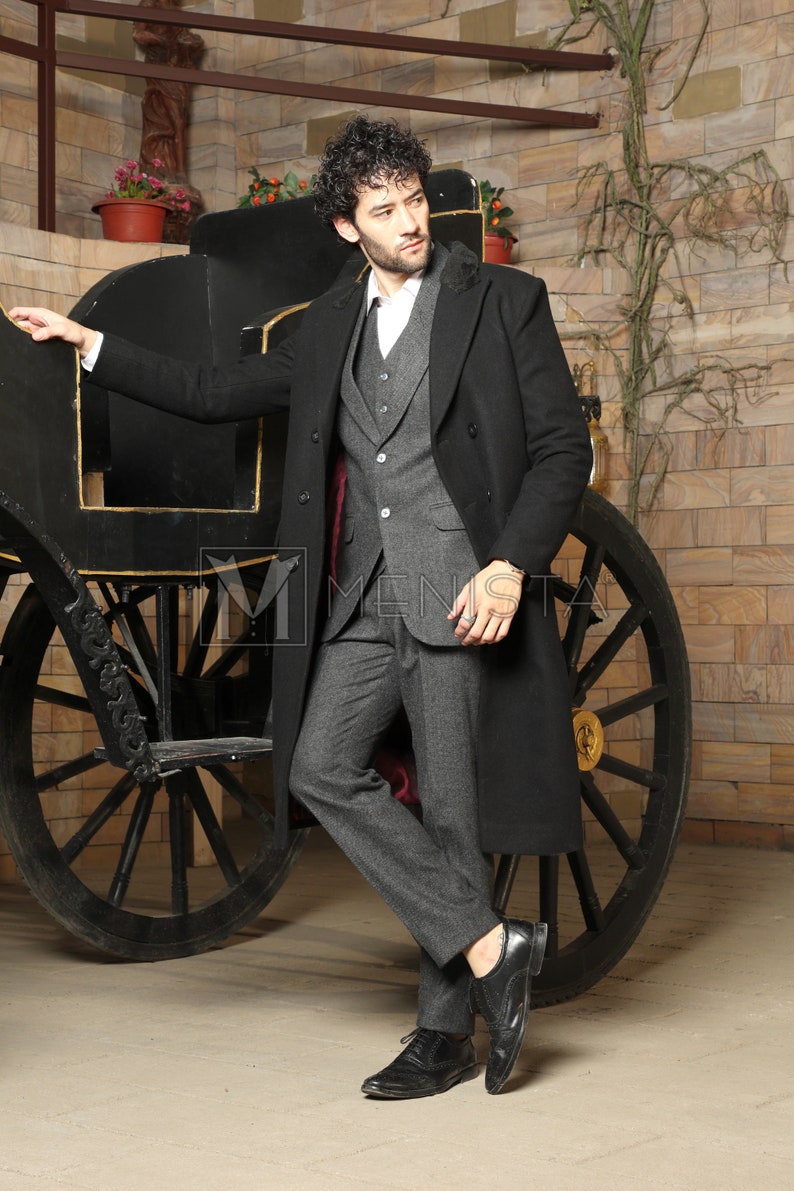 May include: A man wearing a black overcoat with a gray suit and black shoes. He is standing next to a black carriage.