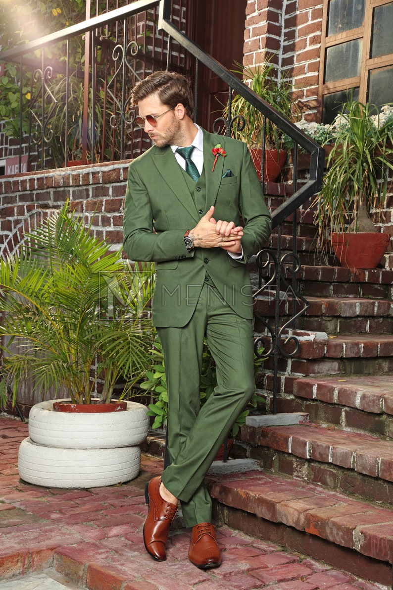 Puede incluir: Un hombre con un traje verde de tres piezas con un cintur&oacute;n de cuero marr&oacute;n y zapatos de cuero marr&oacute;n. Est&aacute; de pie en una escalera de ladrillo con una planta verde en una maceta blanca detr&aacute;s de &eacute;l.