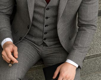 Puede incluir: Un traje gris de tres piezas con corbata y pañuelo de bolsillo burdeos. El traje está hecho de una tela texturizada y tiene un corte clásico.