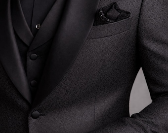 May include: A formal black suit with a patterned texture, featuring a black bow tie, vest, and pocket square. A gold wristwatch with a blue face adds a touch of elegance. The suit has a classic, tailored fit.
