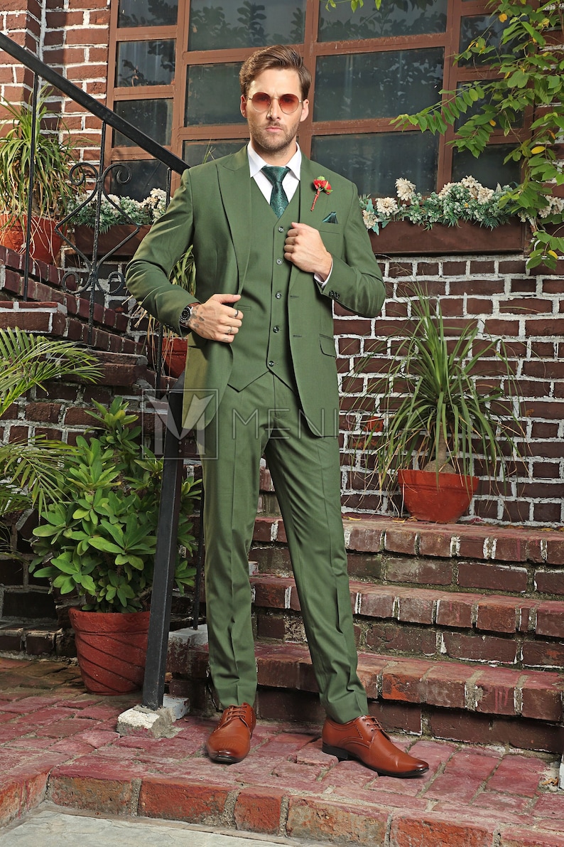 Puede incluir: Un traje de tres piezas en color verde oscuro. El traje incluye una chaqueta, un chaleco y pantalones. El hombre lleva una corbata verde oscuro y zapatos de cuero marr&oacute;n.