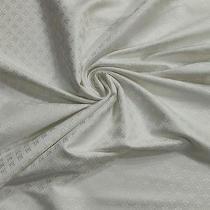 May include: Off-white fabric with a subtle, repeating geometric pattern. The fabric is draped and folded, creating soft shadows and highlights. The texture appears smooth with a slight sheen, suggesting a luxurious material.