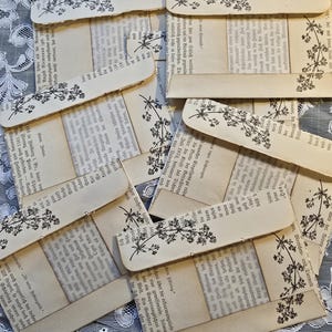 May include: A stack of six vintage-style envelopes with a floral design and a window to view the text inside. The envelopes are made of cream-coloured paper with a brown border. The text inside the envelopes is in German.