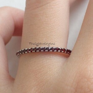 Può includere: Un anello a fascia d'argento con una fila di piccole pietre preziose rosse. L'anello è su un dito.