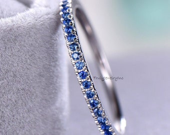 May include: A thin silver band with a row of small blue sapphires set around the entire ring.