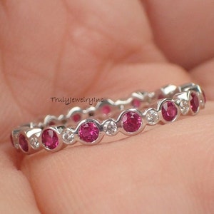 May include: A silver eternity band ring with alternating pink gemstones and small clear diamonds.
