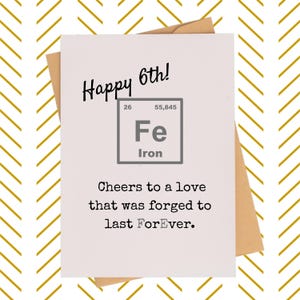 May include: A white greeting card with the text "Happy 6th!" and "Fe Iron" in a box. The card also includes the phrase "Cheers to a love that was forged to last ForEver." The card is inside a brown envelope.