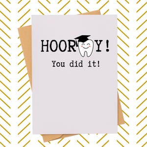 May include: A white graduation card with the text "HOORAY! You did it!" features a smiling tooth wearing a graduation cap. The card is on a brown envelope, set against a gold and white chevron pattern background.