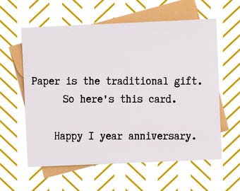 May include: A white greeting card with the text "Paper is the traditional gift. So here's this card. Happy 1 year anniversary." The card is on a brown envelope, set against a gold and white chevron pattern background.