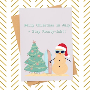 May include: A greeting card with a brown envelope features a snowman wearing sunglasses and a Santa hat, a Christmas tree, and a surfboard on a beach. The card reads "Merry Christmas in July - Stay Frosty-ish!!"