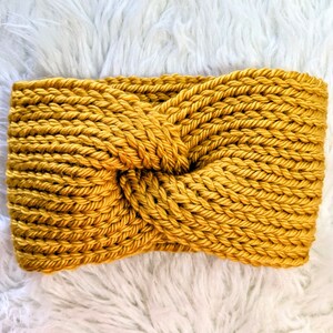 May include: A mustard yellow knitted headband with a knotted design. The headband is made of a soft, chunky yarn.